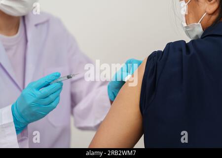 medico che tiene la siringa e che usa il cotone prima di fare l'iniezione al paziente in una maschera medica. Vaccino Covid-19 o coronavirus Foto Stock