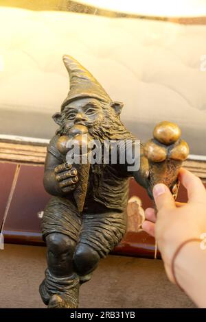 Nana mangia gelato sul davanzale di una vecchia pasticceria. Piccole figure in bronzo di gnomi sulle strade di Breslavia. Europa Figura in bronzo miniatura di uno gnome. Simbolo di Breslavia. Attrazione turistica Foto Stock