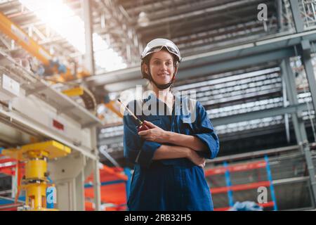 ritrattista donna lavoratrice intelligente professionale in piedi sorriso felice negli interni di grandi edifici industriali. Foto Stock