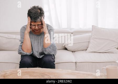 maturo adulto asiatico femminile seduta mani coprire testa sentire male stress mal di testa pensando ansioso problema mentale. il dolore cerebrale senior soffre a casa Foto Stock