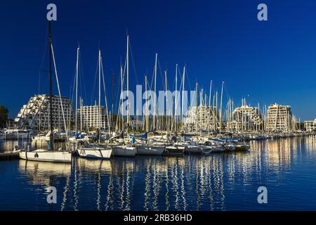 FRANCIA. HERAULT (34) LA GRANDE-MOTTE. BARCHE A VELA NEL PORTO DI FRONTE AGLI EDIFICI PIRAMIDALI Foto Stock