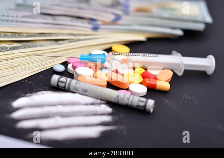 linee di cocaina, siringa, compresse e dollari su un tavolo nero Foto Stock