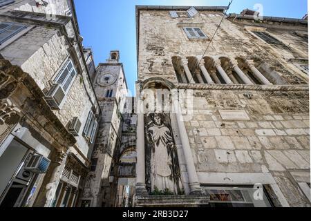 Una scultura di Sant'Antonio Eremita sul Palazzo Ciprianis-Benedetti a Narodni Trg, con la torre dell'orologio romanico del XV secolo e l'ingresso della porta di ferro Foto Stock