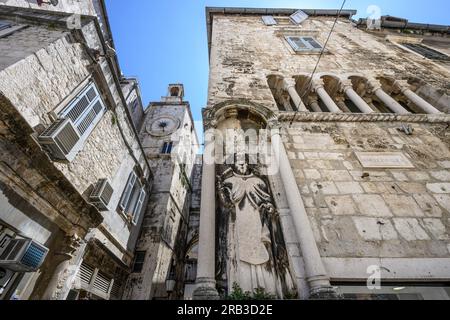 Una scultura di Sant'Antonio Eremita sul Palazzo Ciprianis-Benedetti a Narodni Trg, con la torre dell'orologio romanico del XV secolo e l'ingresso della porta di ferro Foto Stock