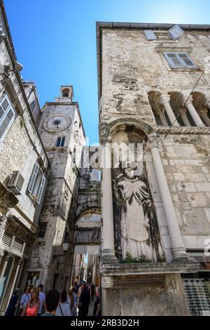 Una scultura di Sant'Antonio Eremita sul Palazzo Ciprianis-Benedetti a Narodni Trg, con la torre dell'orologio romanico del XV secolo e l'ingresso della porta di ferro Foto Stock
