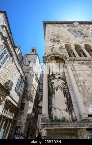 Una scultura di Sant'Antonio Eremita sul Palazzo Ciprianis-Benedetti a Narodni Trg, con la torre dell'orologio romanico del XV secolo e l'ingresso della porta di ferro Foto Stock