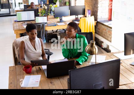 Colleghi afroamericani impegnati che utilizzano tablet e discutono di lavoro in ufficio creativo. Business, brainstorming, tecnologia e lavoro di squadra, inalterati. Foto Stock