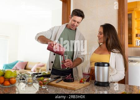 Felice coppia caucasica che serve cocktail di frutta in cucina. Stile di vita sano, cibo e vita domestica, inalterato. Foto Stock