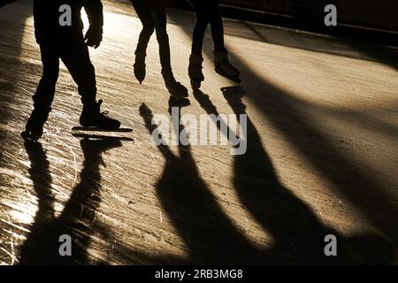 Silhouette di persone sui pattini di ghiaccio in inverno freddo sole Foto Stock