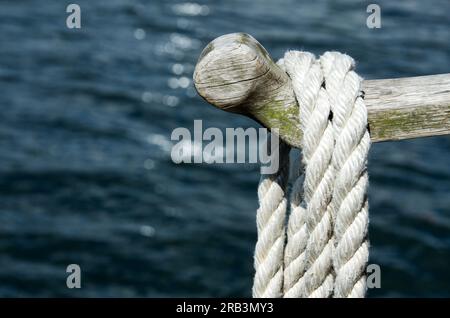 Asta di legno con corda d'ormeggio sospesa sull'acqua in estate. Foto Stock