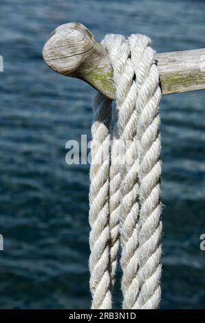 Asta di legno con corda d'ormeggio sospesa sull'acqua in estate. Foto Stock