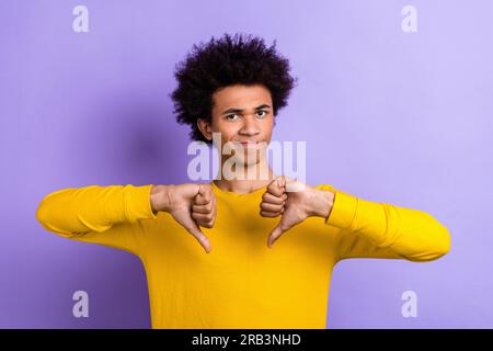 Foto di un giovane ragazzo rigido divertente insoddisfatto che non ama il gesto del pollice verso il basso dimostra la sua valutazione negativa isolata su sfondo di colore viola Foto Stock