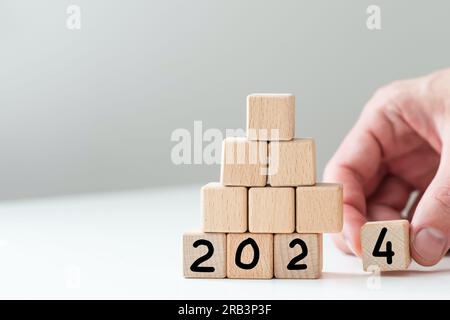 2024 Happy New Year eve blocchi di legno flip change mano sfondo blu. Conto alla rovescia a partire dalla fine del calendario delle azioni 2023 strategia visione futura Foto Stock