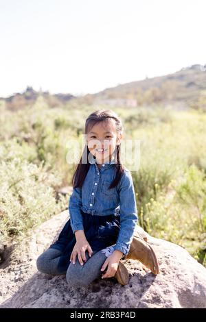 Bambina di sette anni, asiatica, ragazza seduta sul Rock a San Diego Foto Stock