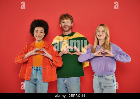 relazione aperta, concetto di poligamia, tre amanti interrazziali che mostrano segno del cuore con le mani sul fondo corallo, diversità culturale, poliamoroso, happ Foto Stock