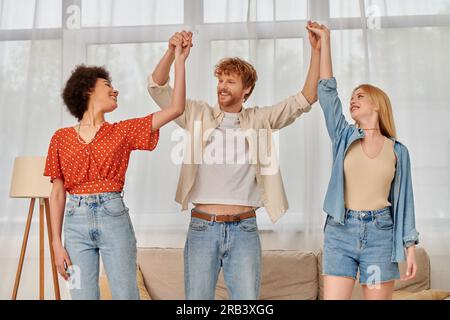 poligamia, tre persone che tengono e alzano la mano in salotto, famiglia alternativa, accettazione e comprensione in relazione, legame Foto Stock
