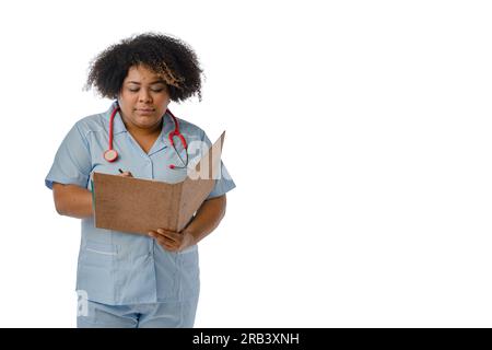 Giovane medico afro-latino in uniforme blu, scrivendo e leggendo file medici in una cartella marrone, sfondo bianco con spazio copia Foto Stock