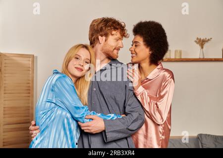 relazioni aperte, uomo felice con i capelli rossi che abbraccia donne interrazziali, diversità culturale, partner non tradizionali, persone multiculturali, accettazione Foto Stock