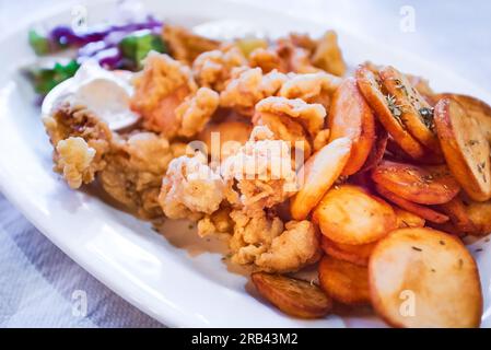 Classico piatto di taverna greca con calamari fritti e patate al forno, menu di pesce sull'isola di Zante, Grecia. Foto Stock