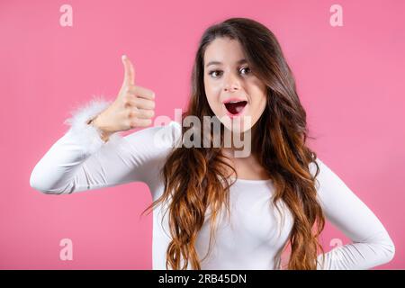 Ritratto di una donna bruna con un ampio sorriso ed emozioni emozionanti, mostrando i pollici in alto sullo sfondo rosa Foto Stock