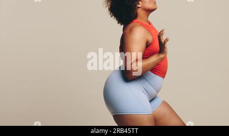 La donna si trova in uno studio di registrazione, indossando abbigliamento sportivo e sfoggiando la sua vestibilità e la sua figura atletica. Donna sportiva in taglia Plus che abbraccia il suo percorso verso la forma Foto Stock