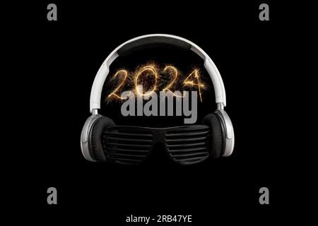 numero 2024 scritto con scintillanti del bengala, cuffie e occhiali da sole a strisce nere su sfondo nero Foto Stock