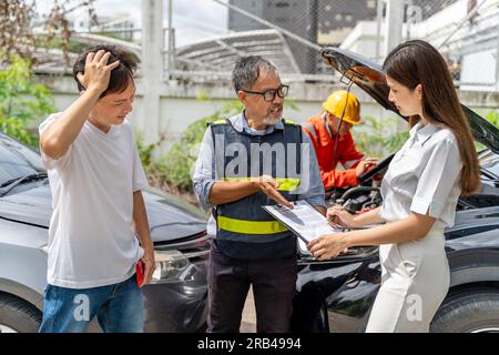 Agente di assicurazione auto che mostra alla sua cliente donna dove firmare il modulo di richiesta di assicurazione contro gli incidenti mentre il colpevole sta vicino a loro a guardare Foto Stock