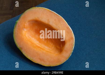 Una foto ravvicinata di un fresco e seducente melone cantaloupe, accentuato da uno sfondo in tessuto blu scuro. La vista dall'alto cattura il suo aspetto rinfrescante Foto Stock