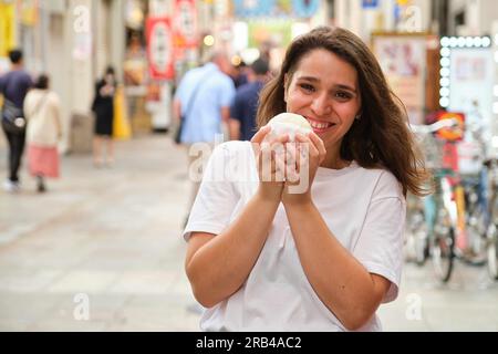 Giovane donna ispanica che mangia nikuman in via Dotonbori a Osaka, in Giappone. Foto Stock