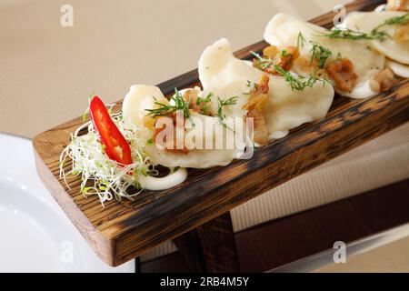 Gnocchi con patate e insalata. Gnocchi con patate e ciccioli in panna acida su un tagliere di legno e insalata. Foto Stock