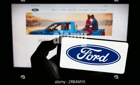 Persona che possiede uno smartphone con il logo del produttore automobilistico statunitense Ford Motor Company sullo schermo davanti al sito Web. Concentrarsi sul display del telefono. Foto Stock