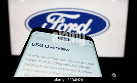 Telefono cellulare con pagina Web del produttore automobilistico statunitense Ford Motor Company sullo schermo davanti al logo aziendale. Mettere a fuoco in alto a sinistra sul display del telefono. Foto Stock