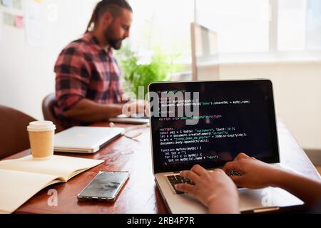 Foto a spalla di una giovane sviluppatrice che scrive codice sul notebook in ufficio Foto Stock