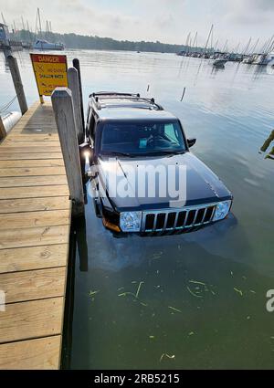 SUV nero mezzo immerso in un lago vicino a un molo di legno Foto Stock