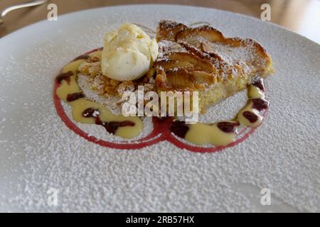 Torta di mele con gelato alla vaniglia. Il dessert italiano è guarnito con crema di lamponi e crema pasticcera Foto Stock