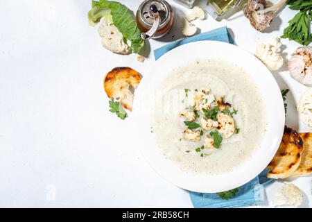 Zuppa di crema di cavolfiori fatta in casa, zuppa vegan di verdure in purea con decorazioni di cavolfiori alla griglia, crostini, formaggio e verdure, tavolo da cucina bianco Foto Stock