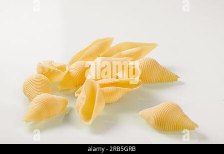 Cucina italiana. Mazzo di pasta a forma di conchiglia su fondo di vetro bianco. Foto Stock