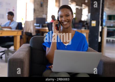 Ritratto di colleghi afroamericani felici che usano il computer e parlano sullo smartphone in ufficio. Business, tecnologia e lavoro di squadra, inalterati. Foto Stock