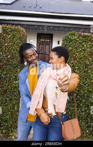 Felice giovane coppia afro-americana che si guarda e si trova all'esterno di una nuova casa con le chiavi. Inalterato, amore, insieme, felice, proprietà di casa, Foto Stock
