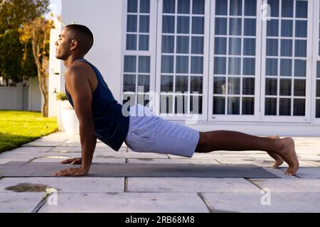 Uomo birazziale concentrato che pratica yoga in un giardino soleggiato. Posa Cobra, estate, benessere, fitness e stile di vita sano, inalterato. Foto Stock