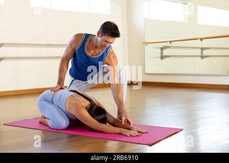 Uomo caucasico che consiglia e donna che pratica yoga in studio. Stile di vita sano, benessere, yoga, relazione, insieme, fitness ed esercizio fisico, unale Foto Stock