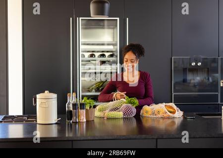 Felice donna birazziale che ha sconfezionato generi alimentari in cucina. Shopping, cibo, stile di vita sano, stile di vita e vita domestica, inalterati. Foto Stock