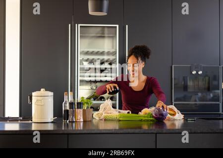 Felice donna birazziale che ha sconfezionato generi alimentari in cucina. Shopping, cibo, stile di vita sano, stile di vita e vita domestica, inalterati. Foto Stock