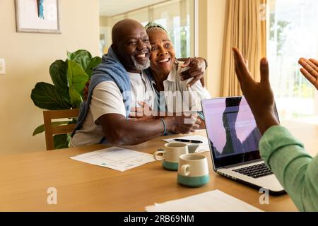 Consulente finanziario maschile afroamericano che utilizza un computer portatile con una felice coppia anziana a casa. Stile di vita senior, finanza, felicità, pensionamento e nazionale l Foto Stock