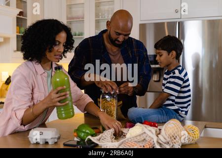 I genitori e i figli birazziali sono felici e hanno fatto la spesa in cucina. Cibo, shopping, stile di vita sano, ecologia, vita familiare e domestica, inalterati. Foto Stock