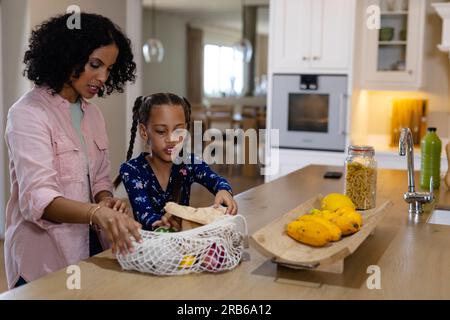 Mamma e figlia birazziali felici che hanno fatto acquisti in cucina e che hanno aperto le valigie per la spesa, spazio fotocopie. Cibo, shopping, stile di vita sano, ecologia, famiglia e domestico Foto Stock