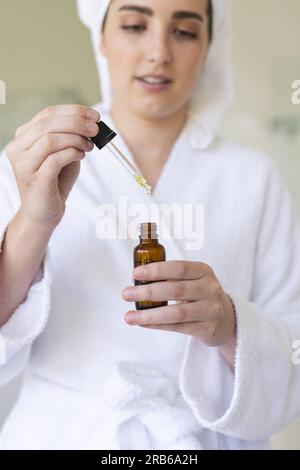 Donna caucasica felice che indossa accappatoio e applica olio in bagno. Vita domestica, cura del sé e stile di vita, inalterato. Foto Stock