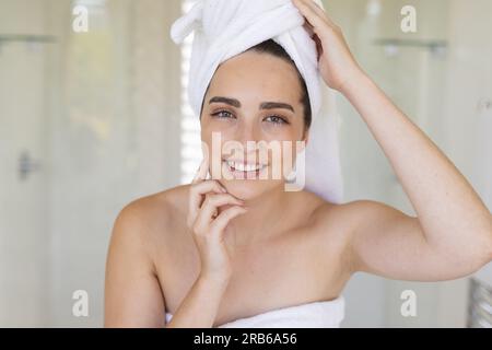 Ritratto di donna caucasica felice con un asciugamano sulla testa in bagno. Vita domestica, cura del sé e stile di vita, inalterato. Foto Stock