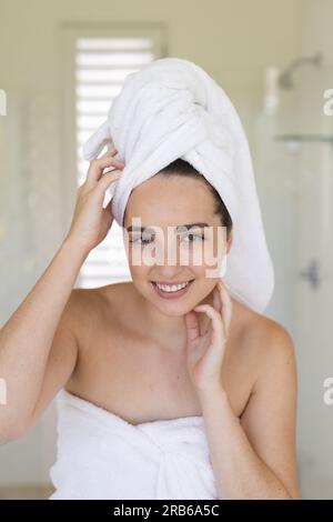 Ritratto di donna caucasica felice con un asciugamano sulla testa in bagno. Vita domestica, cura del sé e stile di vita, inalterato. Foto Stock