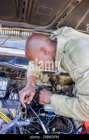 meccanico africano che ripara un'auto d'epoca all'aperto nel cortile Foto Stock
